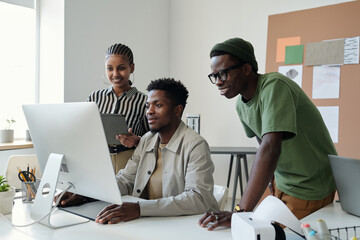 Aufkleber - Three young African American graphic designers looking at computer screen at working meeting while one of them drawing sketch