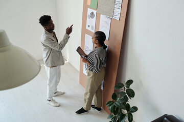 Aufkleber - Young confident businessman pointing at one of papers with graphic drawings on noticeboard while explaining something to colleague