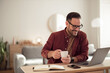 © Jelena - Businessman drinking his first morning coffee, having an online meeting, being at home office.
