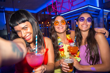 Fun of friends smiling with glasses of alcohol in a nightclub taking a selfie at a night party