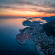 Amazing aerial panoramic view of the picturesque town of Dubrovnik with the old town, illuminated streets and buildings and marina with boats at fiery sunset.