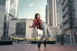© Diego Zarulli - Photo shoot of stylish caucasian hip hop dancer posing on her toes with red shirt, jeans and black boots shoes and top with a urban town as background. City shooting of moving model bending the back