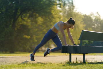 Wall Mural - Full lenght portrait of beautiful fitness woman doing mountain clibers exercise against park bench.