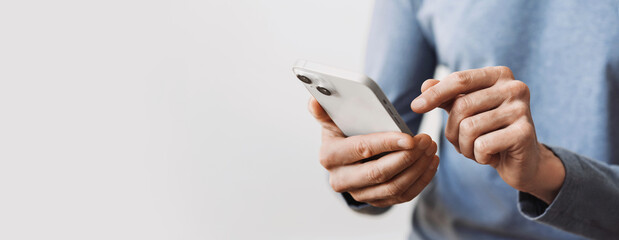 closeup of adult male hand using mobile phone, young man texting on smartphone over grey background,