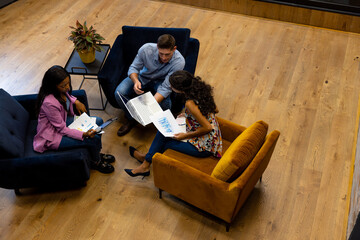 High angle view of diverse male and female colleagues in discussion using laptop in office lounge