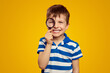 © Davidovici - Adorable child smiling and examining environment with magnifying glass against yellow background, wearing blue striped polo shirt.