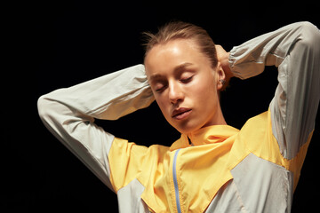 Wall Mural - Young fitness girl getting ready for a workout at the stadium. Attractive slender blonde in a yellow-gray sports jacket is focused on training. Active lifestyle. Close up shot.