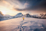 Mountaineer walking with footprint in snow storm and sunrise over snowy mountain in Senja Island