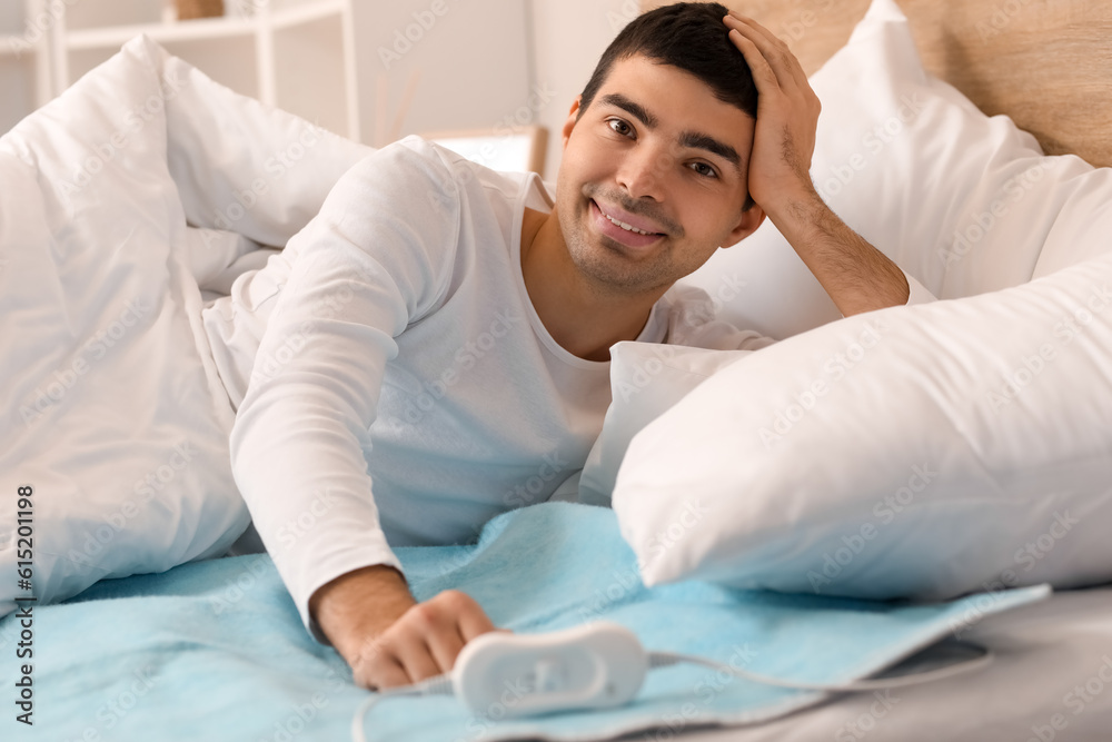 Young man lying on electric heating pad in bedroom