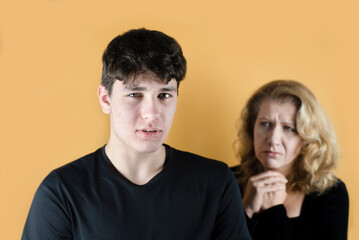 A young guy, teenager, tries to justify his bad behavior in front of mother, who is standing next to him and is upset because of a misunderstanding with her son, a problem in communication