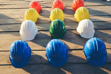 Wall Mural - Safety helmet (hard hat) for engineer, safety officer, or architect, place on wooden floor. Yellow, White, green, blue, and orange safety hat (helmet) on construction site.