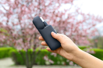 Female hand holding modern electronic cigar outdoors