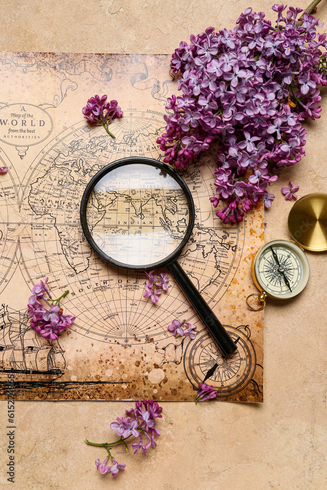 World map with compass, magnifier and lilac flowers on beige grunge background