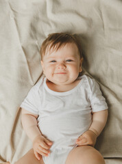 charming blue-eyed 6-month-old baby lies in bed in a white bodysuit. view from above