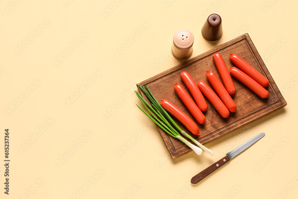 Board with tasty thin sausages and green onion on beige background