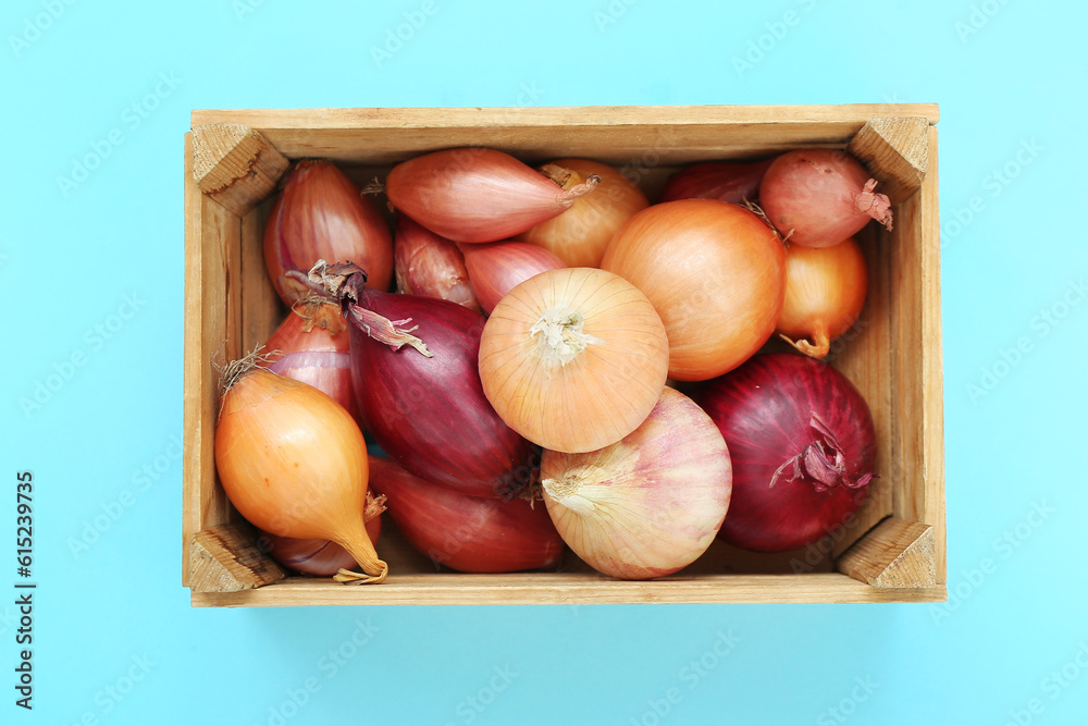 Wooden box with different kinds of onion on blue background