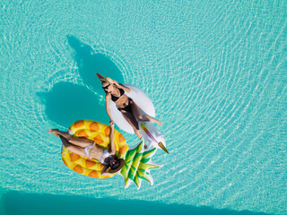 Wall Mural - Top view of female friends wearing bikini lying on an inflatable toy in pool. Woman sunbathing on floating pool inflatable toy.