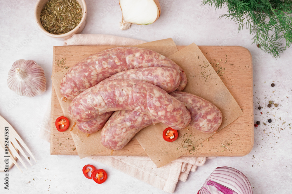 Wooden board with raw homemade sausages on light background