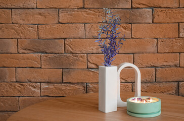 Wall Mural - Beautiful branches and burning candle on table near brick wall in room, closeup