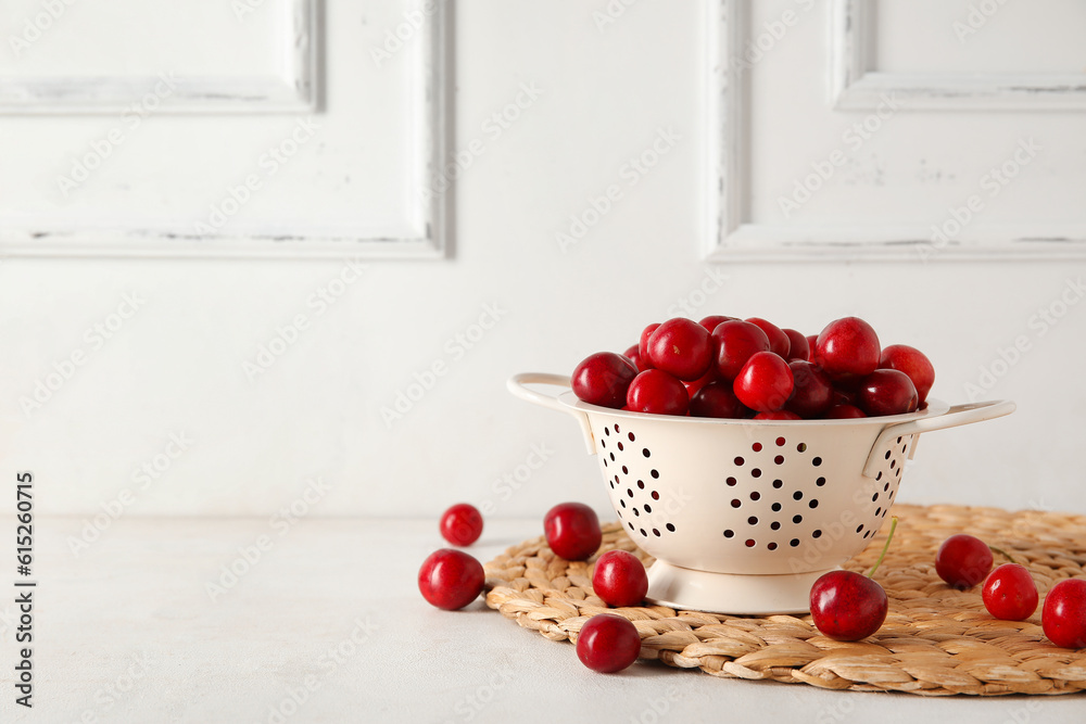 Colander with sweet cherries on white background