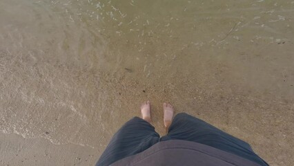 Wall Mural - Looking down at feet on the shore of a sandy beach 