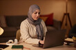© Seventyfour - Young Muslim businesswoman in hijab and casualwear typing on laptop keyboard while sitting by workplace in home office and networking