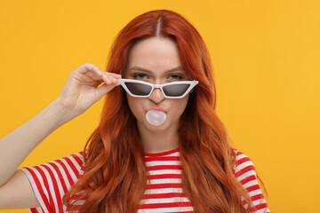 Wall Mural - Beautiful woman in sunglasses blowing bubble gum on orange background