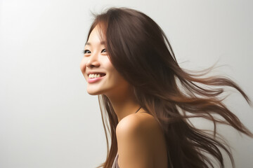 Charming Asian teenager with long hair blowing in the breeze exudes positivity with a bright smile on a white background.