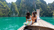 Group of Young Asian woman friends sitting on wooden boat passing tropical island beach in sunny day. Attractive girl enjoy outdoor lifestyle travel ocean on summer holiday vacation at Krabi, Thailand