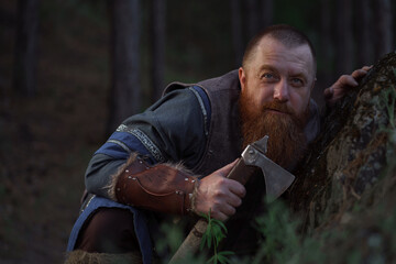 Lurking medieval red-haired viking warrior with beard with an ax in forest