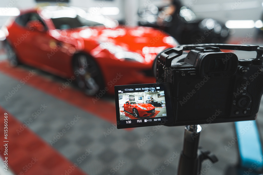 Professional car photo session at mechanic's or in car detailing studio. Digital photo camera taking picture of a red car. Blurred background. High quality photo