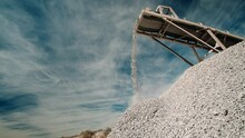 Conveyor Belt Of A Rock Crusher Dumping Aggregate In Slow Motion Onto A Pile Under A Blue Sky With Clouds