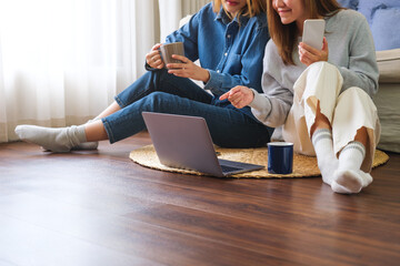 Wall Mural - Closeup image of a young couple women using mobile phone and laptop computer together