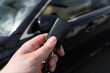 © Longfin Media - Hand of man holding remote car key, next to a black vehicle.