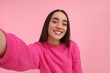 © New Africa - Smiling young woman taking selfie on pink background