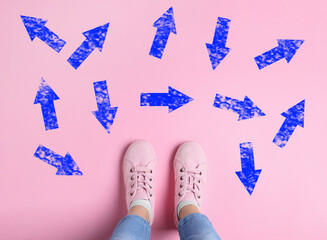 Wall Mural - Choosing future profession. Girl standing in front of drawn signs on pink background, top view. Arrows pointing in different directions symbolizing diversity of opportunities