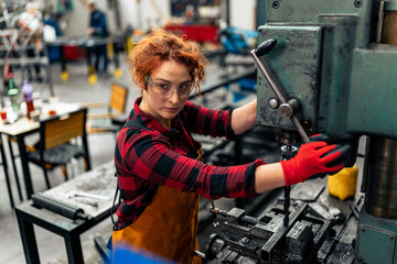 A young woman in STEM adjusts a machine with a drill before starting work on a new project, uses protective equipment and practices safe work