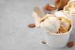 Scoops of ice cream with caramel sauce in paper cup on light grey table, closeup. Space for text