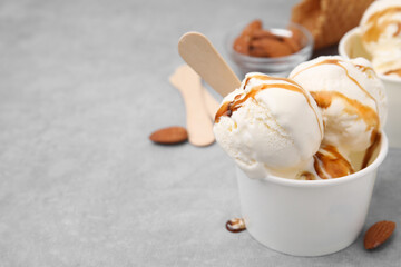 Wall Mural - Scoops of ice cream with caramel sauce in paper cup on light grey table, closeup. Space for text