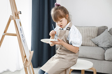 Girl with Down syndrome wearing beige apron painting on an easel