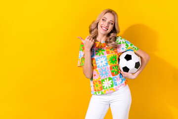 Wall Mural - Photo of adorable cute girl dressed colorful t-shirt holding football ball indicating look empty space isolated on yellow color background