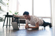 © BullRun - Young man doing plank exercise with laptop in living room