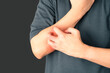 Man scratching arm from having itching over dark background. Cause of itchy skin include  eczema, atopic dermatitis, psoriasis, food or drugs allergies and dry skin. Health care concept.