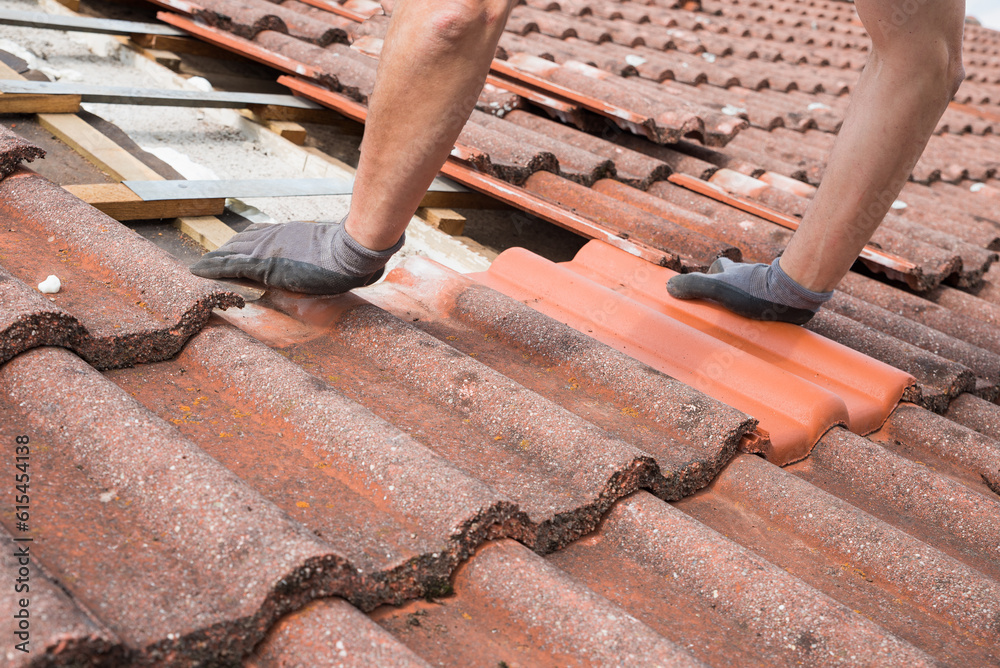 man replaces broken roof shingles on the rooftop with new ones