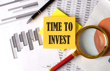 Poster - TIME TO INVEST text on a sticky on the graph background with pen and magnifier