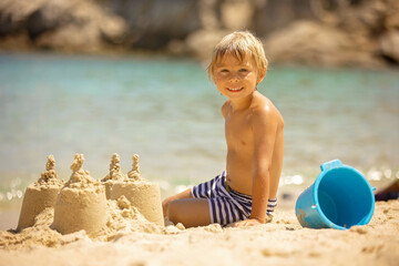 Wall Mural - Happy child on the beach, building sand castle, enjoying summer, playing. Greece