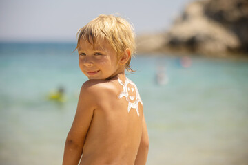 Sticker - Happy child, blond boy on the beach with applied sun screen,  enjoying summer, playing. Chalkidiki