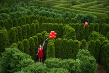 Balloons Drift Away From A Young Woman In A Garden Maze; Luray, Virginia, United States Of America