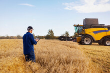 Farmer using a tablet to manage his grain harvest with a combine working in the background; Alcomdale, Alberta, Canada