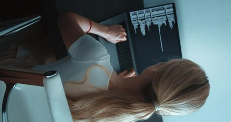Vertical video, rear view of woman programmer developer looking at computer monitor and writing program code sitting at workplace. IT software developer typing data coding programming with laptop.